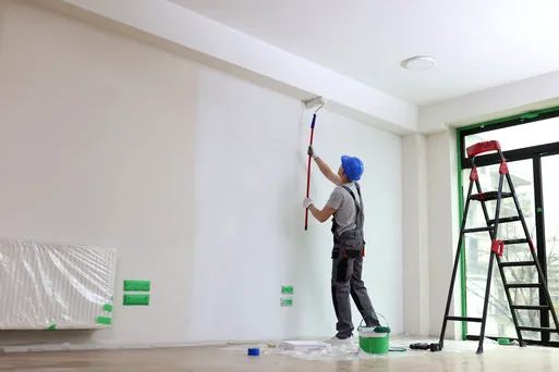 Painter rolling a fresh coat on a bare white wall in an empty room