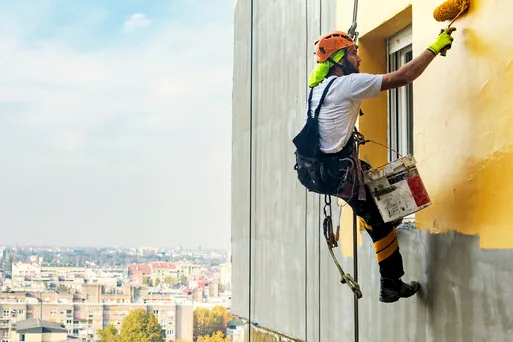 Painter on ropes painting a tall wall